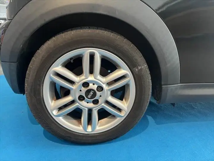 Gros plan sur la roue avant gauche d'une MINI Cooper cabriolet noire avec jante argentée à six branches.