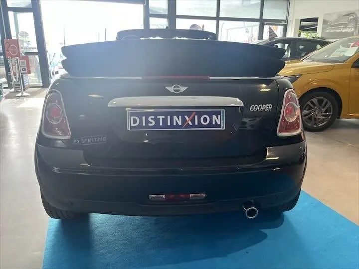 Vue arrière d'une MINI Cooper cabriolet noire avec capote relevée, en intérieur de showroom.