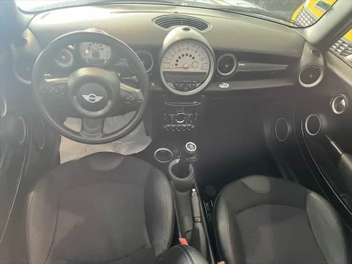 Vue intérieure avant de la MINI Cooper Cabriolet noire de 2012, avec tableau de bord rond et volant multifonction en cuir.