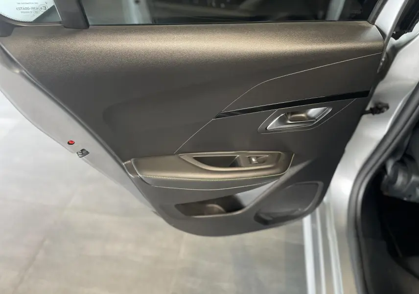 Vue rapprochée de la porte arrière gauche noire avec poignée argentée d'une Peugeot 208 gris clair métallisé.