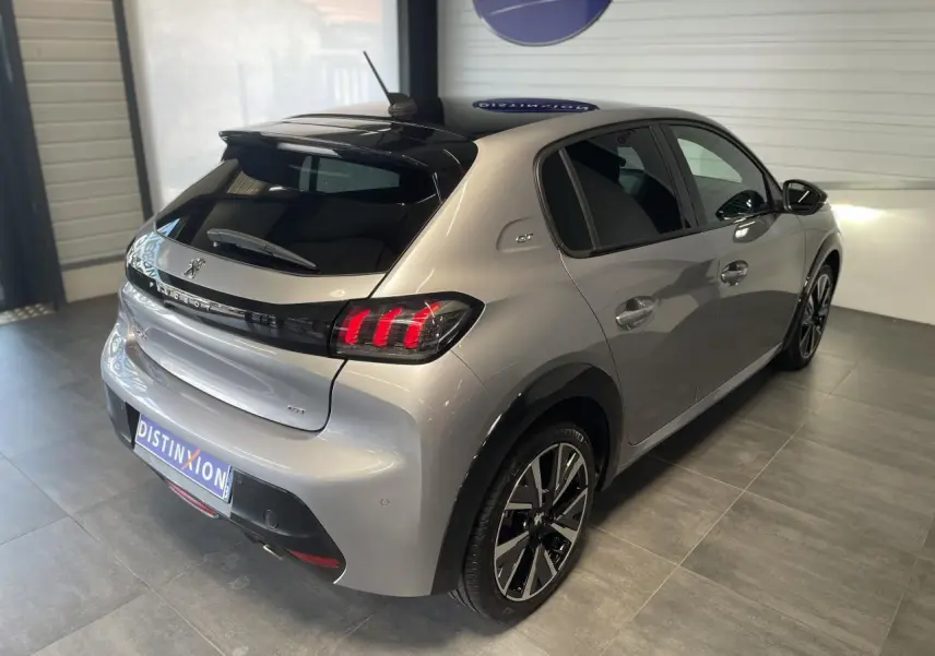 Vue 3/4 arrière droite d'une Peugeot 208 gris clair métallisé avec toit noir et jantes alliage 17 pouces Bronx.
