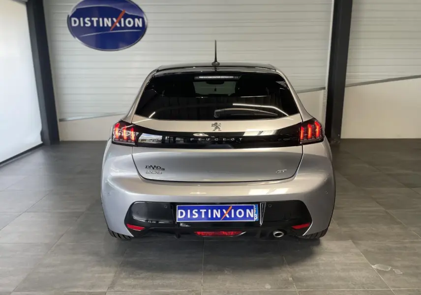 Vue arrière d'une Peugeot 208 gris clair métallisé avec toit noir et feux arrière LED en intérieur showroom.