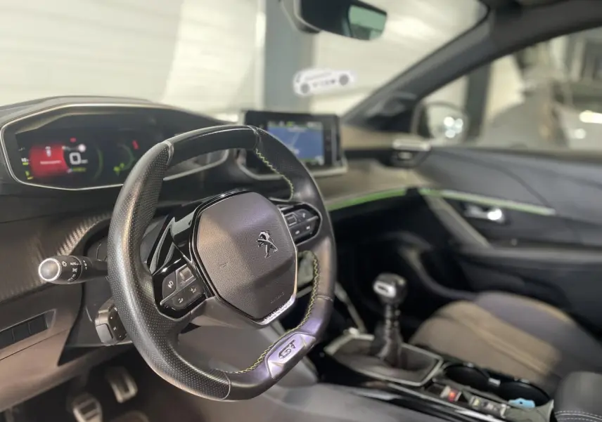 Intérieur Peugeot 208 GT 2023 vu côté conducteur, volant cuir noir avec surpiqûres vertes et tableau de bord numérique.
