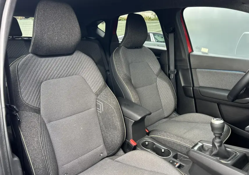 Vue intérieure sur les sièges avant gris avec surpiqûres, accoudoir central et levier de vitesse manuel du Renault Captur rouge.
