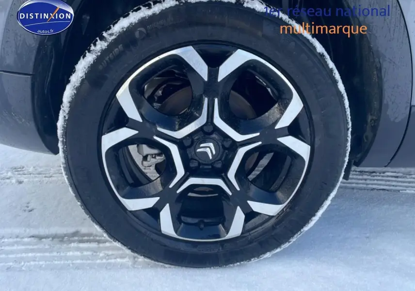 Gros plan sur la jante alu noire et argentée d’un Citroën C5 Aircross gris platinium, avec neige autour du pneu.