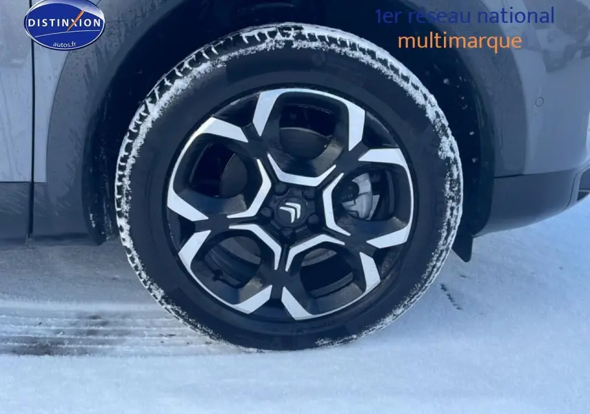 Gros plan sur la roue avant droite du Citroën C5 Aircross gris platinium avec jante alu noire et argentée, neige au sol.