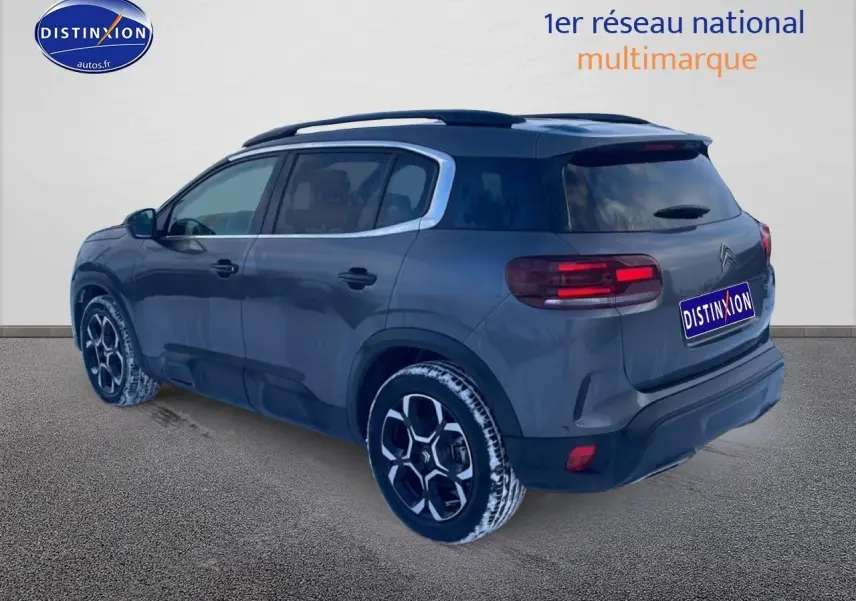 Vue 3/4 arrière droite du Citroën C5 Aircross gris platinium avec jantes alu et barres de toit visibles.