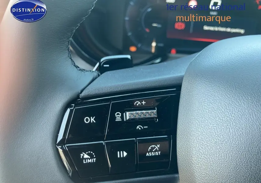 Gros plan sur les commandes au volant de l'Alfa Romeo Junior 1.2 hybride ivoire et noir, affichage digital en arrière-plan.