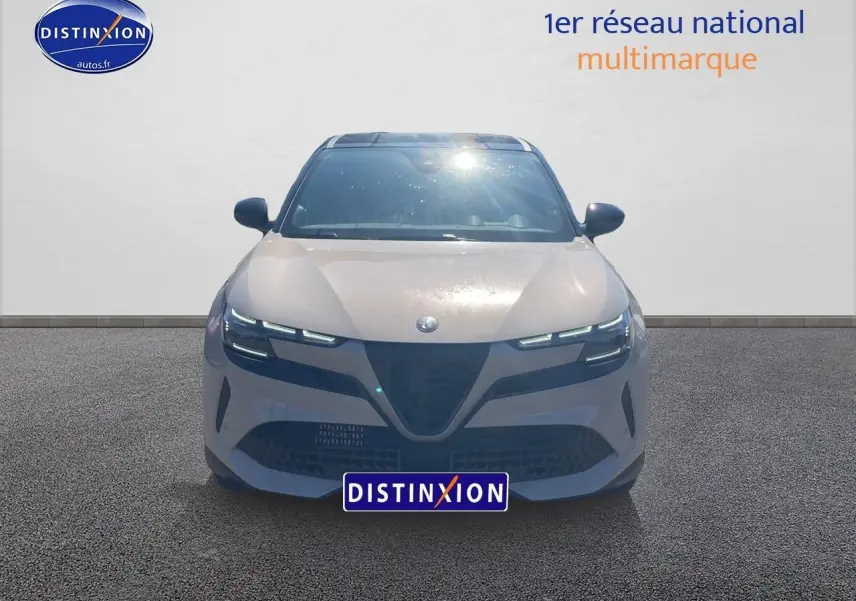 Vue frontale d'une Alfa Romeo Junior 1.2 hybride ivoire et noir avec phares matrix LED allumés sur fond neutre.