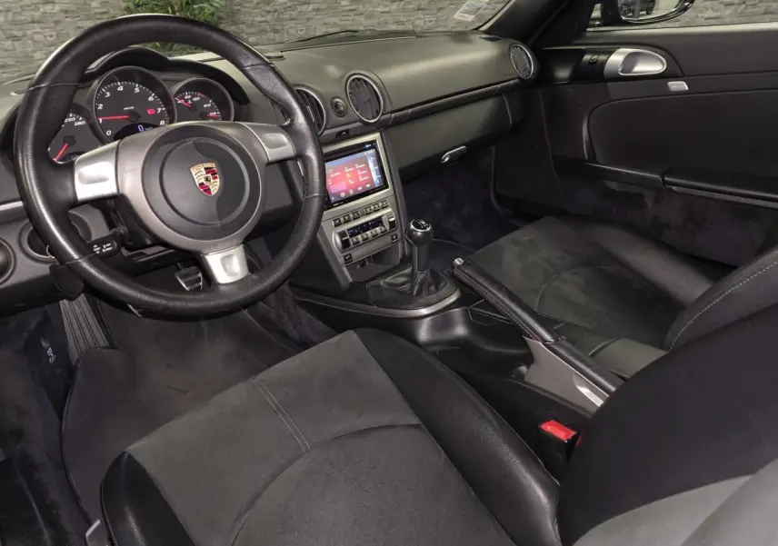 Intérieur noir de Porsche Cayman 2.7i 2008 vu côté conducteur, volant cuir et console centrale avec boîte manuelle.
