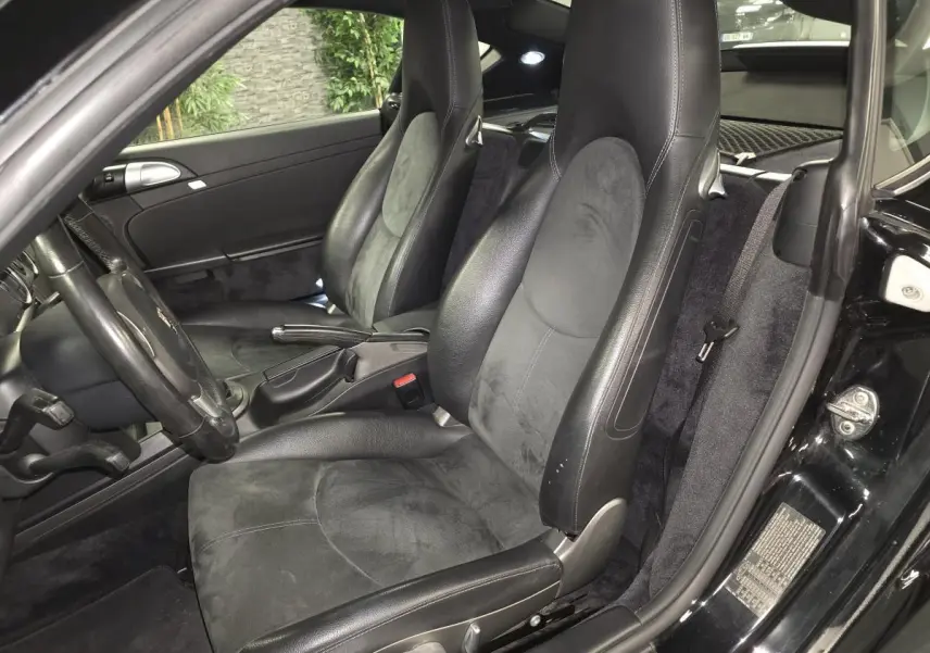 Vue intérieure côté gauche de la Porsche Cayman 2.7i noire de 2008, avec sièges sport en cuir et alcantara.