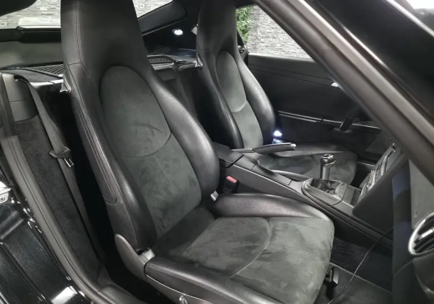 Vue intérieure côté droit de la Porsche Cayman 2.7i noire de 2008, sièges sport en Alcantara et cuir avec levier de vitesses manuel.