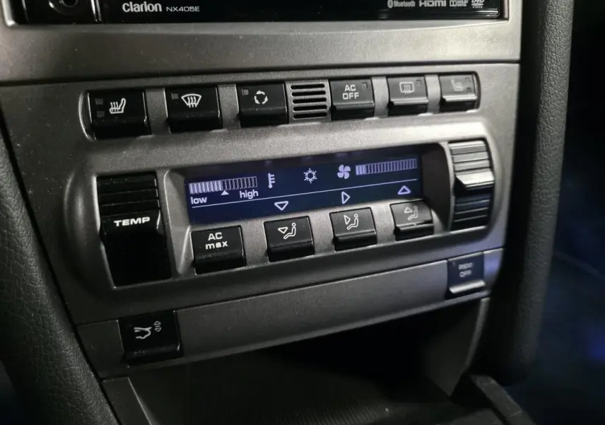 Détail de la console centrale noire de la Porsche Cayman 2.7i 2008 avec commandes climatisation et boutons de réglage.