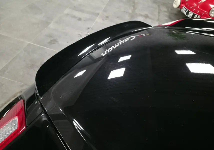 Vue rapprochée arrière gauche d’une Porsche Cayman 2.7i noire avec aileron arrière déployé et feu arrière rouge.