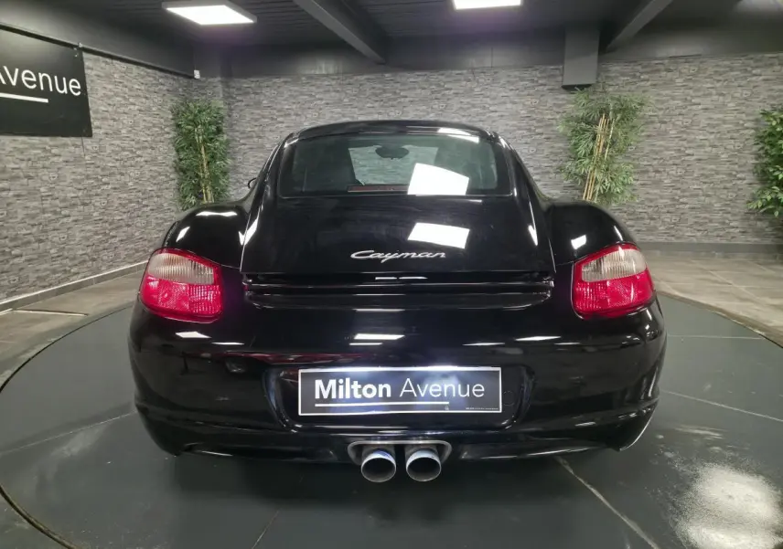 Vue arrière d'une Porsche Cayman 2.7i noire de 2008 avec double sortie d'échappement centrale et feux rouges.