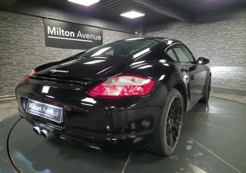 Vue 3/4 arrière droite d'une Porsche Cayman 2.7i noire avec jantes SportDesign noires et double sortie d'échappement centrale.