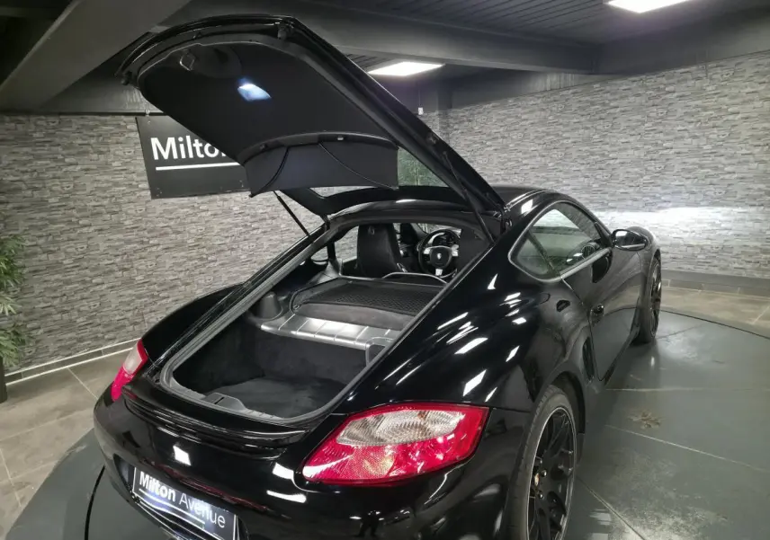 Vue 3/4 arrière droite d'une Porsche Cayman 2.7i noire avec coffre arrière ouvert et jantes SportDesign noires.