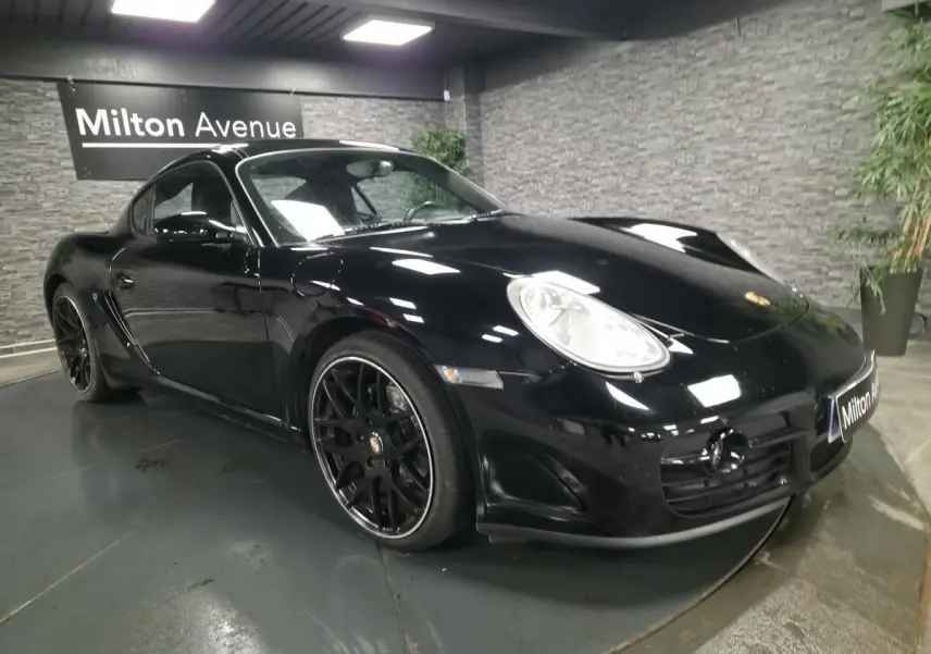 Porsche Cayman 2.7i noire vue 3/4 avant droit avec jantes SportDesign noires de 19 pouces dans un showroom.