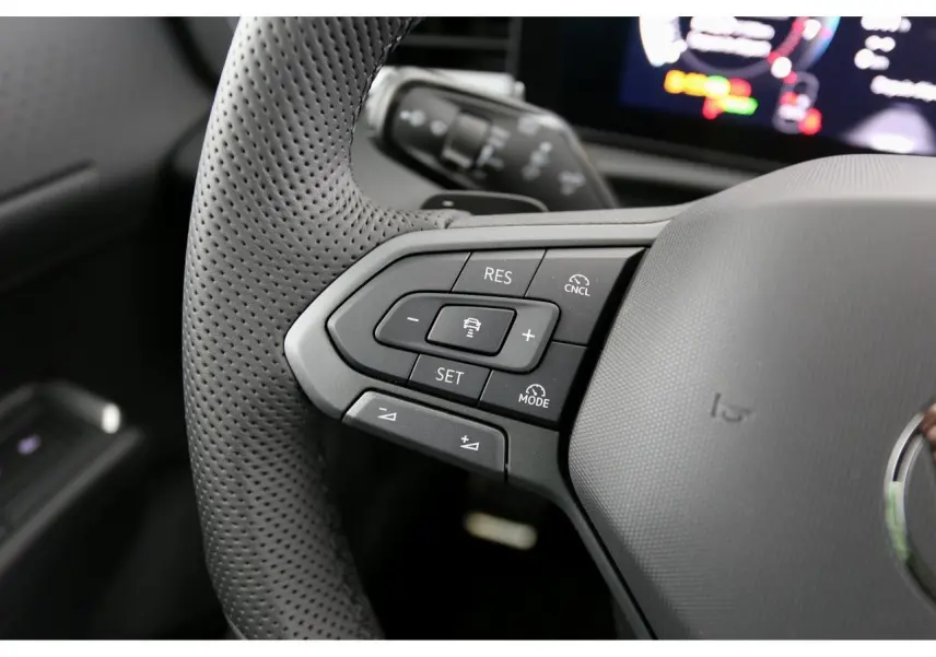 Gros plan sur les commandes gauche du volant perforé du Volkswagen T-Roc 2026, intérieur noir avec affichage numérique flou.