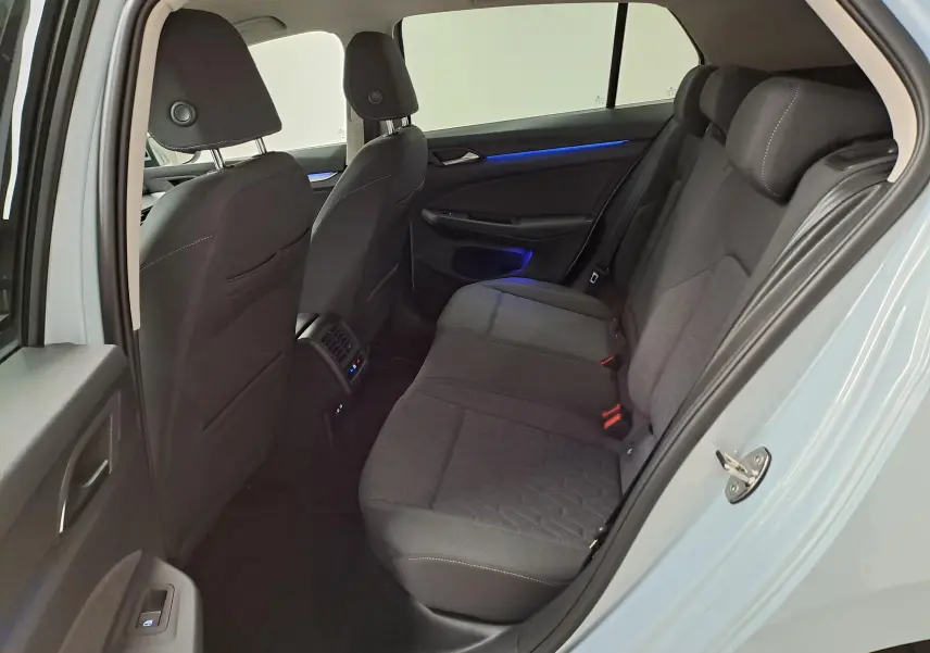 Vue intérieure arrière côté gauche de la Volkswagen Golf 1.5 eTSI 116 DSG7 Bleu Glacier avec sièges tissu gris et éclairage d'ambiance bleu.