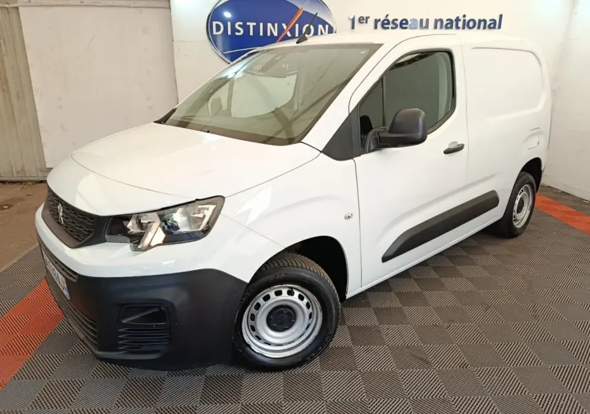 Vue 3/4 avant droit d’un Peugeot Partner blanc 2022 avec pare-chocs noirs et jantes acier en intérieur showroom.