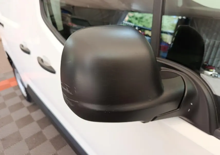Gros plan sur le rétroviseur noir côté droit d’un Peugeot Partner blanc vu de profil avant.