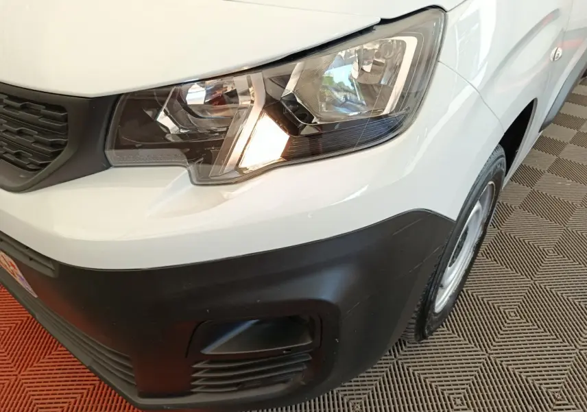 Vue rapprochée du phare avant droit d’un Peugeot Partner blanc avec pare-chocs noir et jante acier.