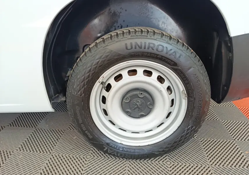 Gros plan sur la roue avant droite blanche d’un Peugeot Partner blanc, avec jante acier et logo Peugeot central.