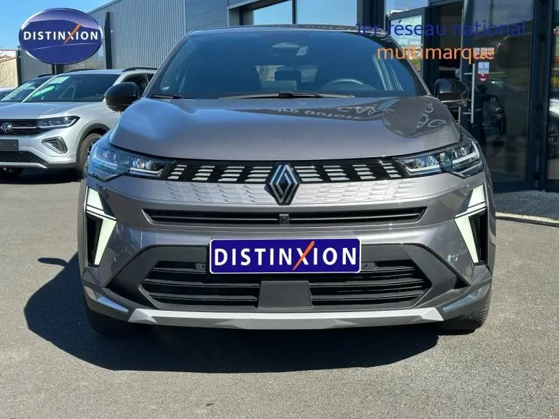 Vue de face d'une Renault Symbioz grise avec calandre chromée et phares LED fins, plaque Distinxion visible.