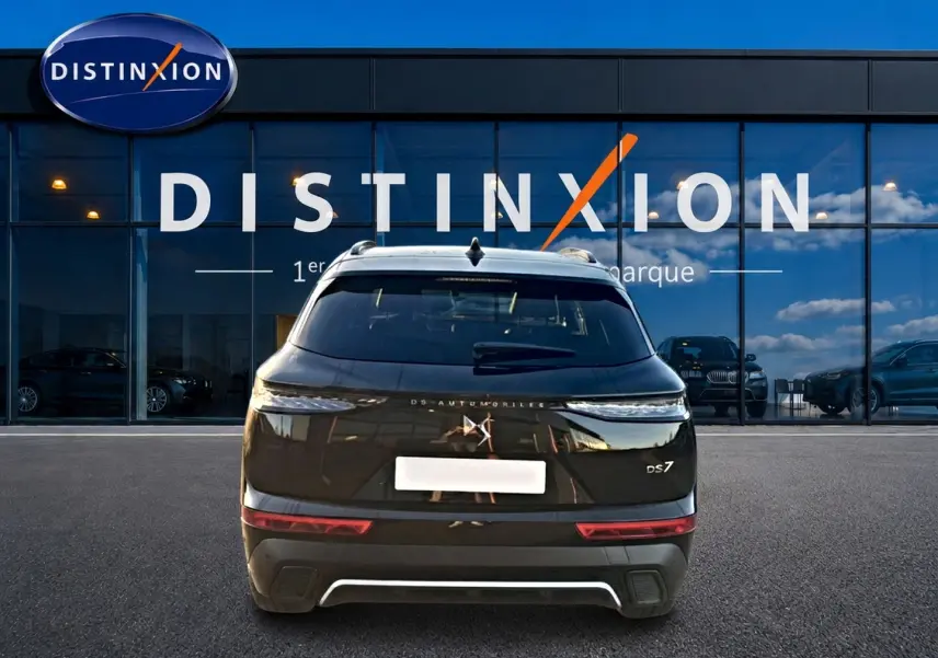 Vue arrière d'un DS7 noir 2026 avec feux LED fins et logo DS distinctif, stationné devant une vitrine Distinxion.