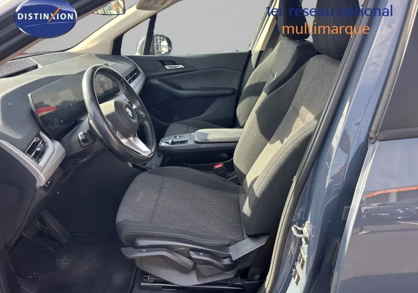 Vue intérieure côté conducteur d'une BMW Série 2 Active Tourer 218d 2023 avec sièges tissu gris et volant cuir, porte ouverte.