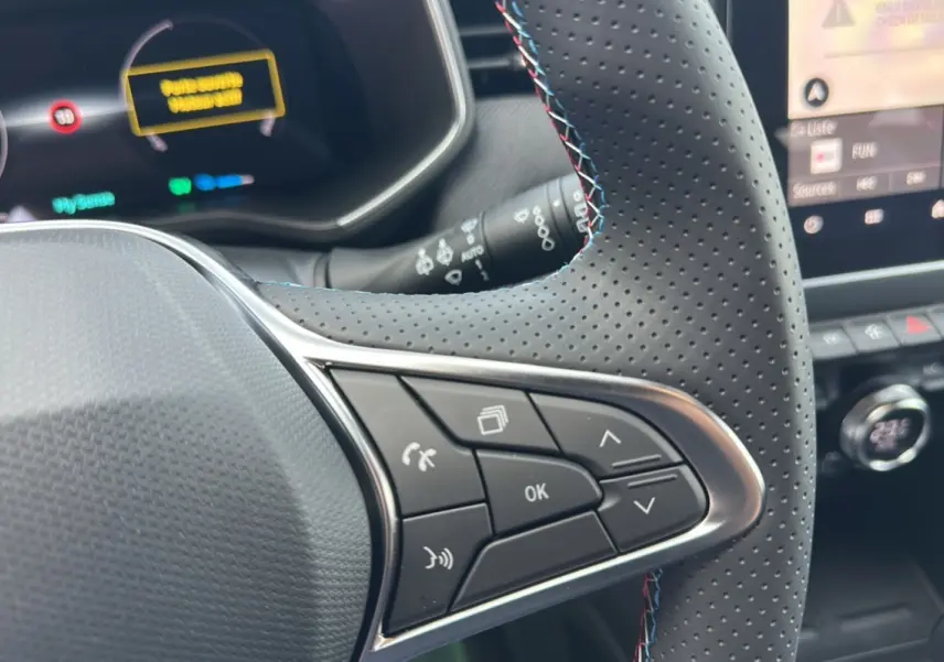 Gros plan sur le volant cuir perforé à commandes multifonctions de la Renault Clio Gris Rafale 2025, tableau de bord numérique en arrière-plan.