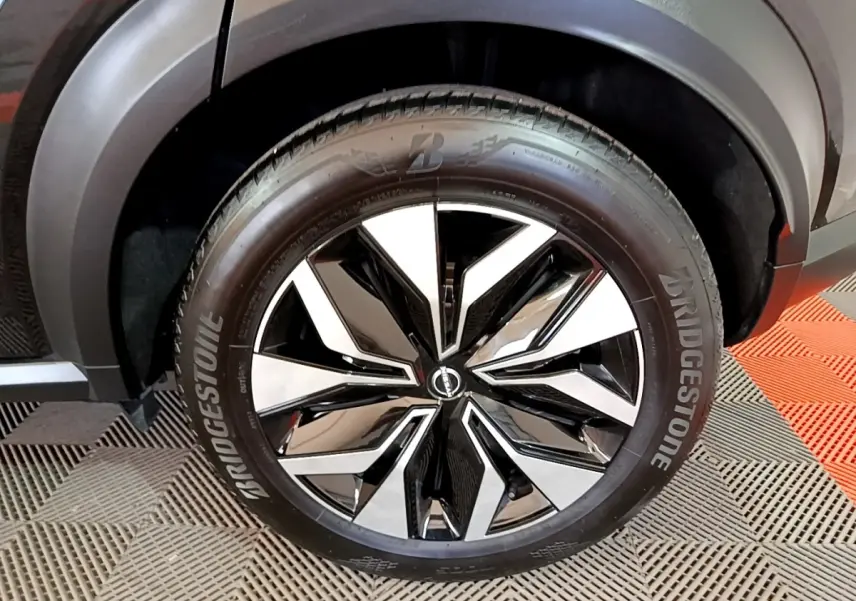 Gros plan sur la roue avant droite noire du Nissan Juke 2023 avec jante alliage bicolore et pneu Bridgestone.