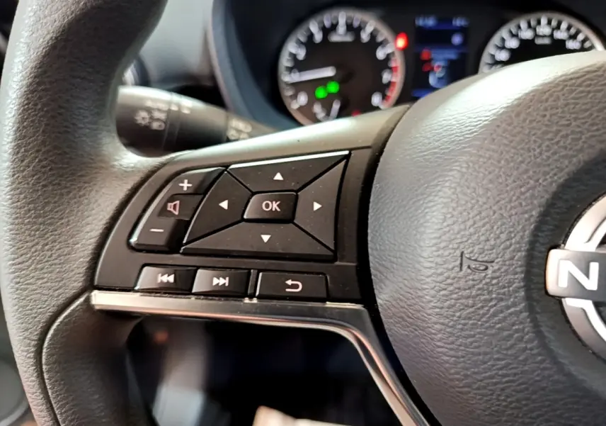 Gros plan sur les commandes multifonctions au volant noir du Nissan Juke 2023 avec tableau de bord et compteurs en arrière-plan flous.