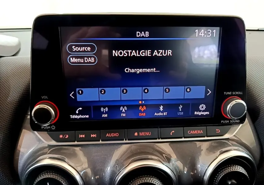 Écran tactile central du Nissan Juke noir 2023 affichant la radio DAB avec commandes audio et climatisation en dessous.