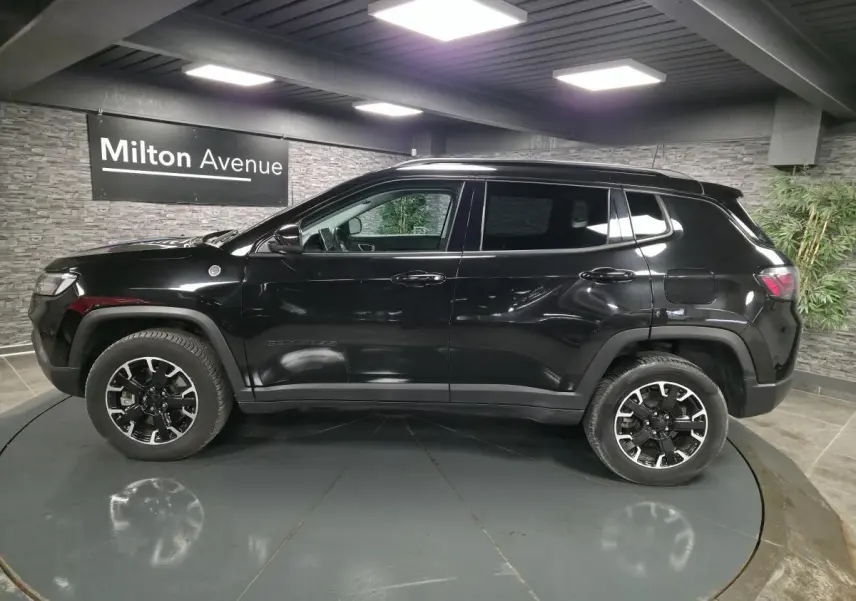 Profil côté gauche d'un Jeep Compass Trailhawk noir brillant, avec jantes alliage noires et toit assorti.