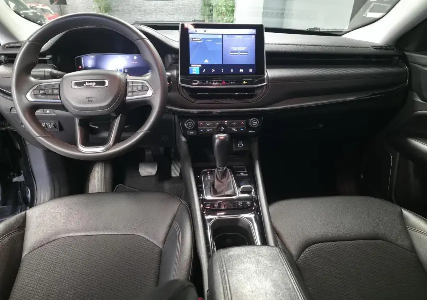 Vue intérieure avant du Jeep Compass Trailhawk 2022, tableau de bord noir avec écran tactile central et volant multifonction.