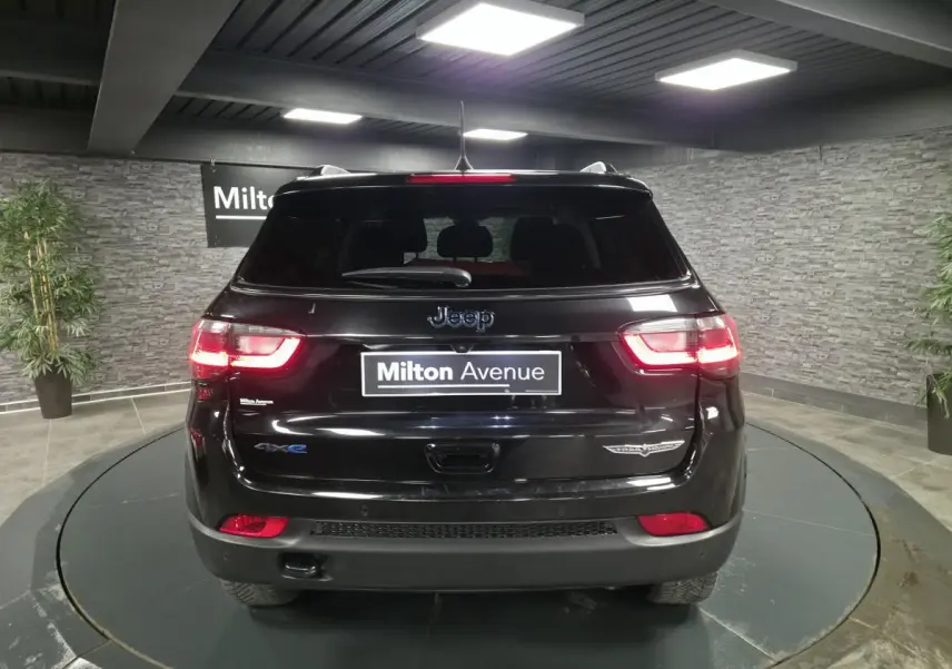 Vue arrière d'un Jeep Compass Trailhawk noir brillant avec feux LED allumés dans un showroom.
