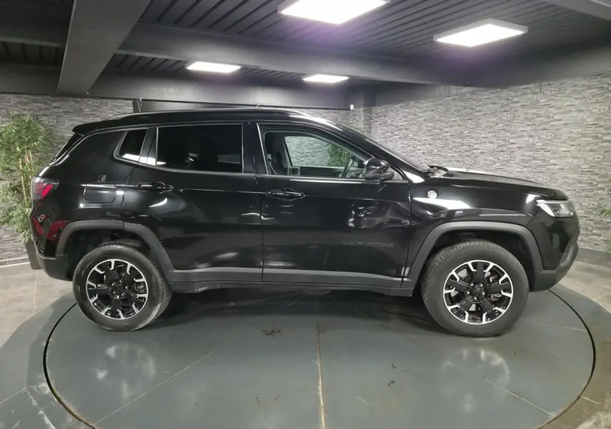 Vue latérale droite d'un Jeep Compass Trailhawk noir avec jantes alliage noires et vitres surteintées dans un showroom.