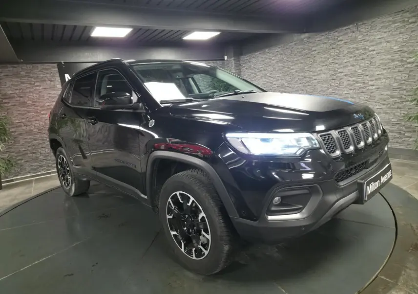Jeep Compass Trailhawk noir vu en 3/4 avant droit avec phares allumés dans un showroom.