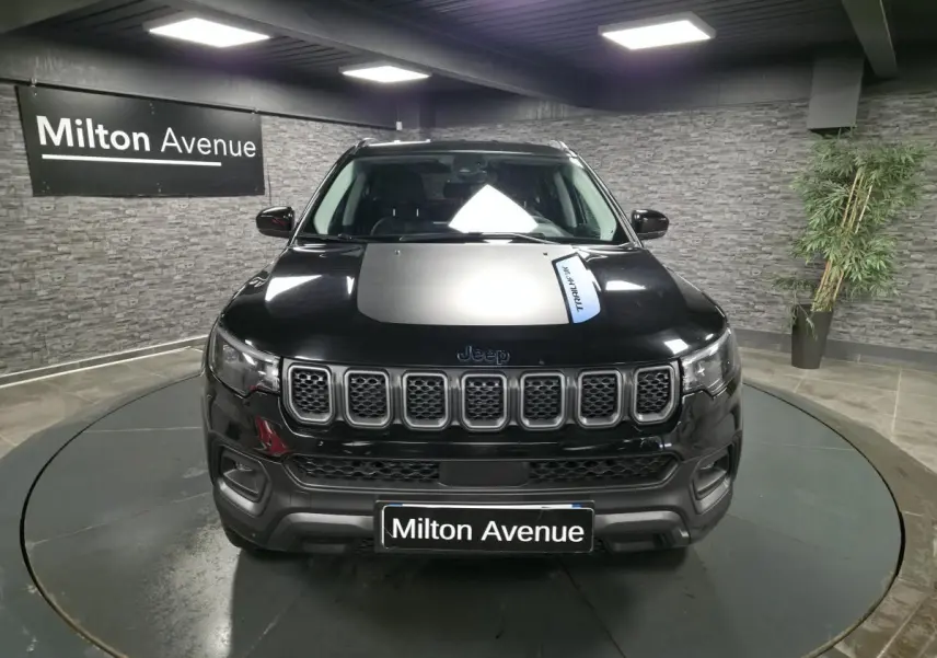 Vue avant d'un Jeep Compass Trailhawk noir avec sticker Trailhawk sur le capot, en intérieur showroom.