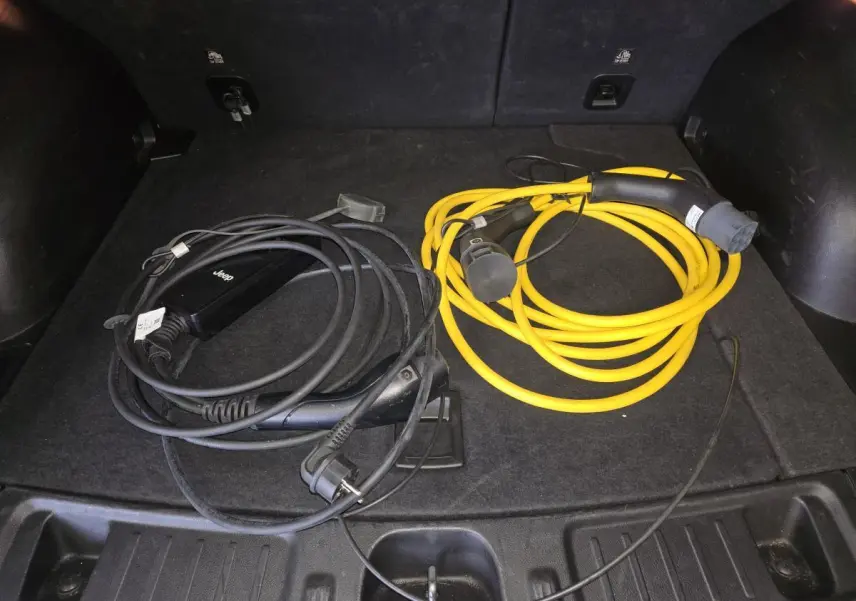 Coffre ouvert d’un Jeep Compass noir 2022 montrant deux câbles de recharge hybride, un noir et un jaune.