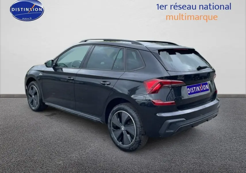 Vue 3/4 arrière droite d'un Skoda Kamiq noir avec jantes alu et barres de toit, sur fond neutre.
