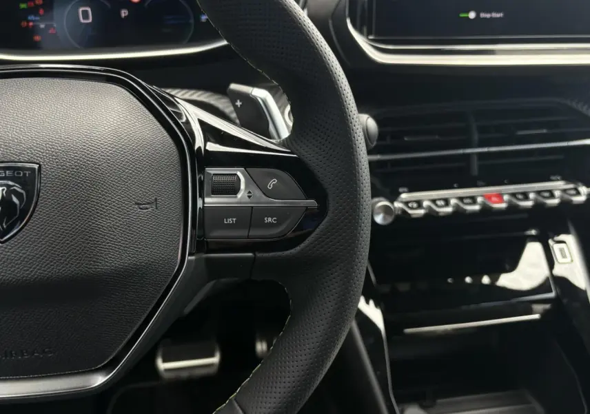 Gros plan sur le volant cuir perforé et la console centrale noire brillante du Peugeot 208 Hybrid 110 e-DSC6 GT.