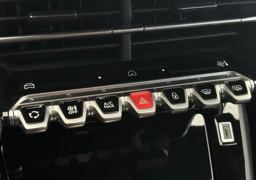 Gros plan sur la rangée de boutons de commande métalliques et noirs avec un bouton rouge au centre dans l’habitacle noir du Peugeot 208 Hybrid 110 GT.