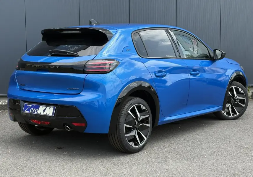 Vue 3/4 arrière droite d’une Peugeot 208 Hybrid 110 GT bleu Vertigo avec jantes alliage bi-tons et toit noir.