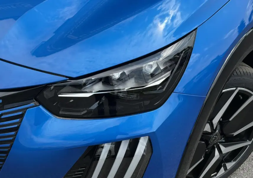 Gros plan sur l'avant droit bleu Vertigo du Peugeot 208 Hybrid 110 e-DSC6 GT, mettant en valeur le phare LED et la jante alliage diamantée.