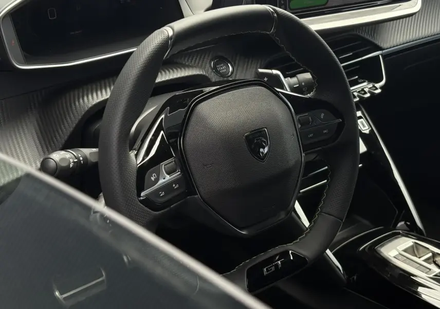 Vue rapprochée du volant compact cuir noir avec badge GT et commandes intégrées dans l’habitacle du Peugeot 208 Hybrid 2025.