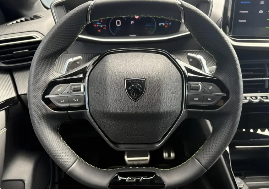 Volant cuir perforé Peugeot 208 Hybrid GT vu de face avec badge GT et commandes intégrées, intérieur noir et surpiqûres vertes.