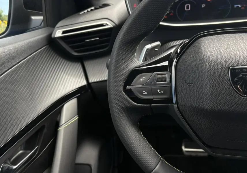 Vue rapprochée du volant cuir perforé avec commandes multimédia et tableau de bord numérique de la Peugeot 208 Hybrid GT.